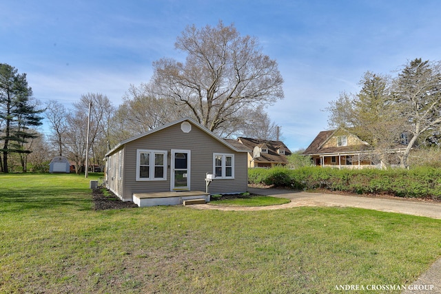 rear view of property featuring a lawn, an outdoor structure, and a storage unit