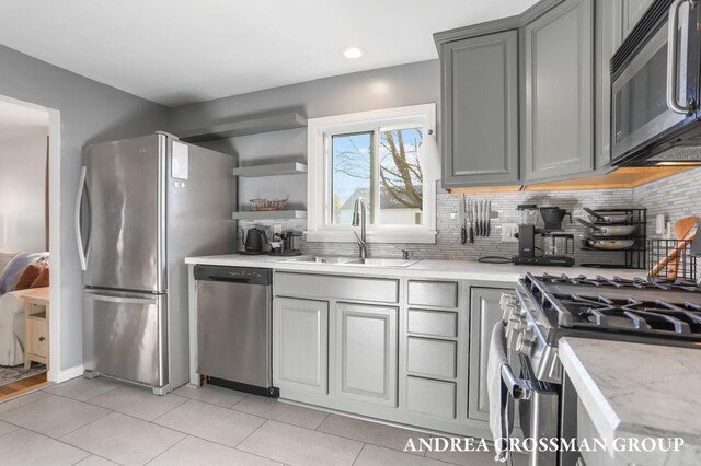 kitchen with backsplash, appliances with stainless steel finishes, a sink, light tile patterned floors, and gray cabinetry