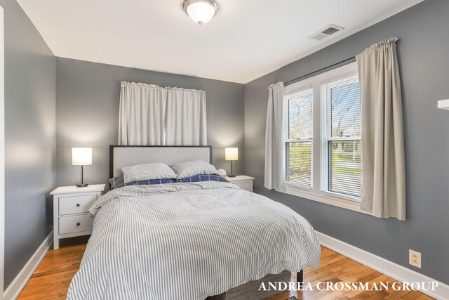 bedroom featuring baseboards, light wood finished floors, and visible vents