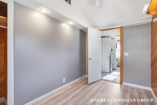 unfurnished bedroom with visible vents, stacked washer and clothes dryer, lofted ceiling, baseboards, and light wood finished floors