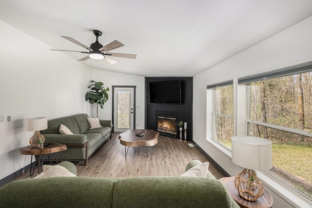 living area with a fireplace, a ceiling fan, baseboards, wood finished floors, and lofted ceiling