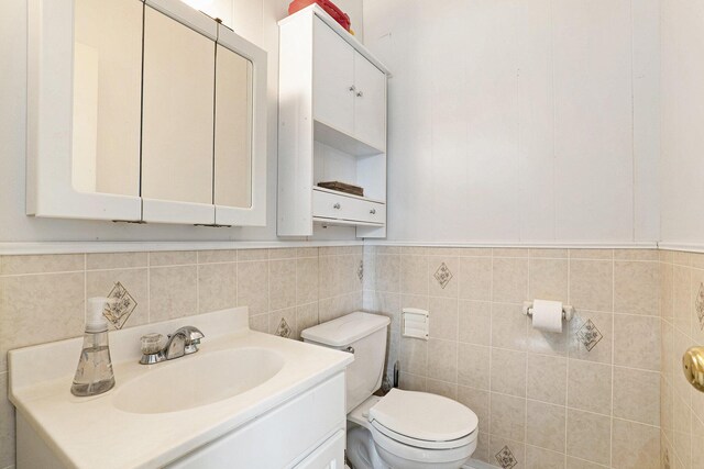 half bathroom featuring toilet, tile walls, and vanity