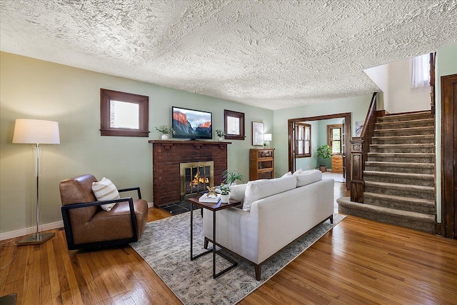 living area with wood-type flooring, a textured ceiling, a brick fireplace, and stairway