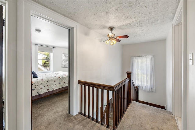 hallway with a textured ceiling, carpet, and an upstairs landing