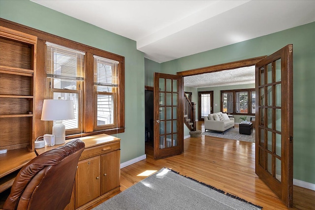 office space with baseboards, french doors, and light wood-type flooring