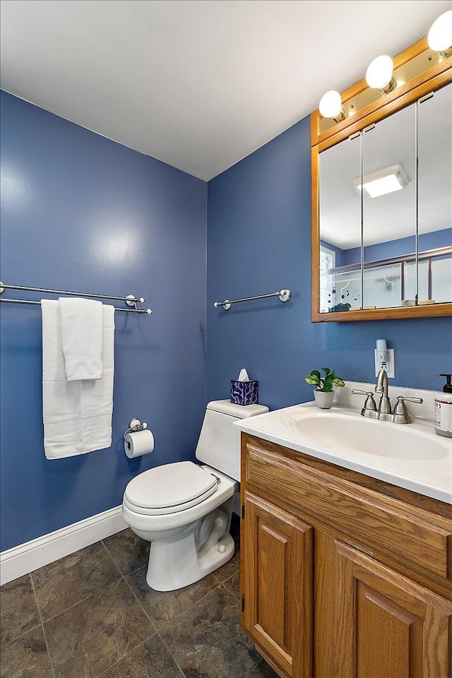 bathroom featuring baseboards, stone finish floor, vanity, and toilet