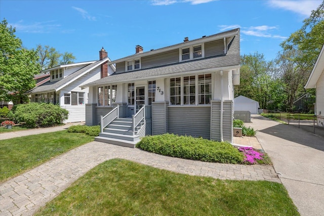 view of front facade featuring a porch, a chimney, an outdoor structure, a front lawn, and a shingled roof
