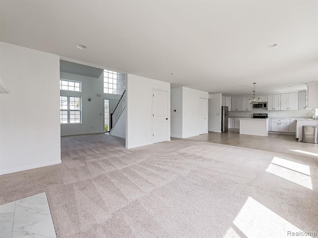 unfurnished living room with baseboards, a sink, stairs, and light colored carpet