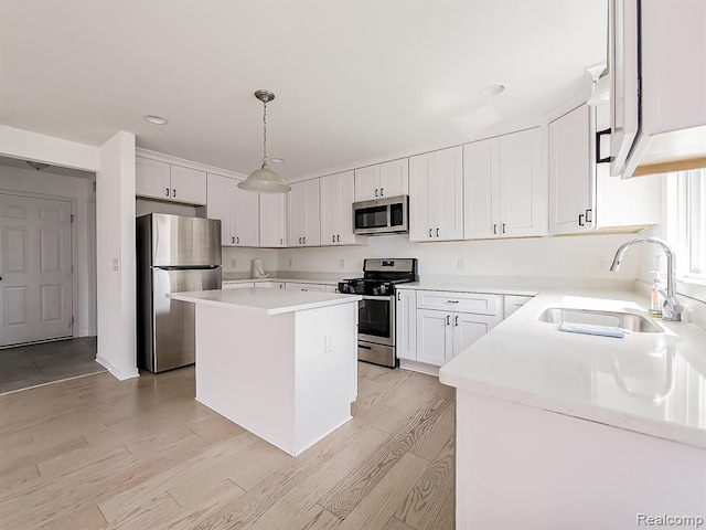 kitchen with a kitchen island, a sink, light wood finished floors, hanging light fixtures, and stainless steel appliances