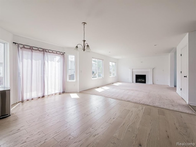 unfurnished living room featuring baseboards, a fireplace, light wood finished floors, and a chandelier