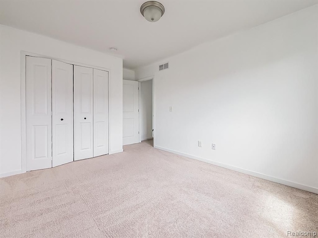 unfurnished bedroom featuring baseboards, light carpet, a closet, and visible vents