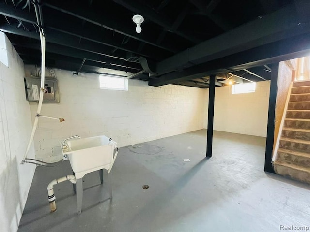 basement featuring stairway, plenty of natural light, electric panel, and a sink