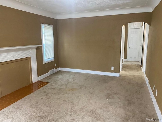 unfurnished living room with arched walkways, carpet, and baseboards