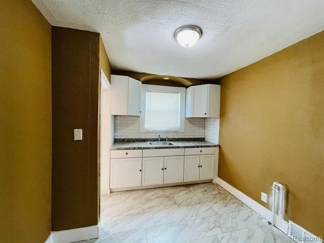 kitchen featuring light marble finish floors, backsplash, a sink, white cabinetry, and baseboards