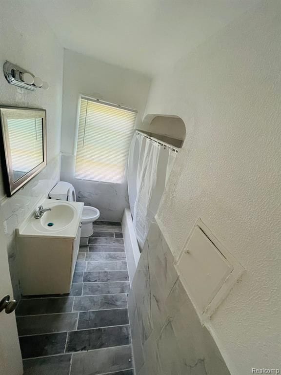 full bath with toilet, vanity, curtained shower, and a textured wall