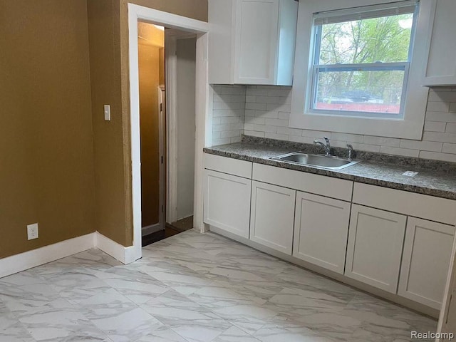 kitchen featuring a sink, light marble finish floors, baseboards, and tasteful backsplash