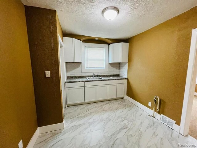 kitchen featuring a sink, light marble finish floors, dark countertops, white cabinetry, and backsplash