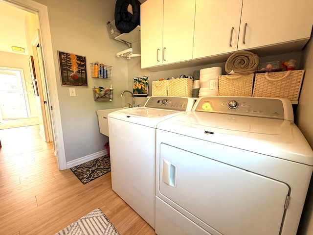 laundry room with baseboards, washer and clothes dryer, light wood-style flooring, a sink, and cabinet space