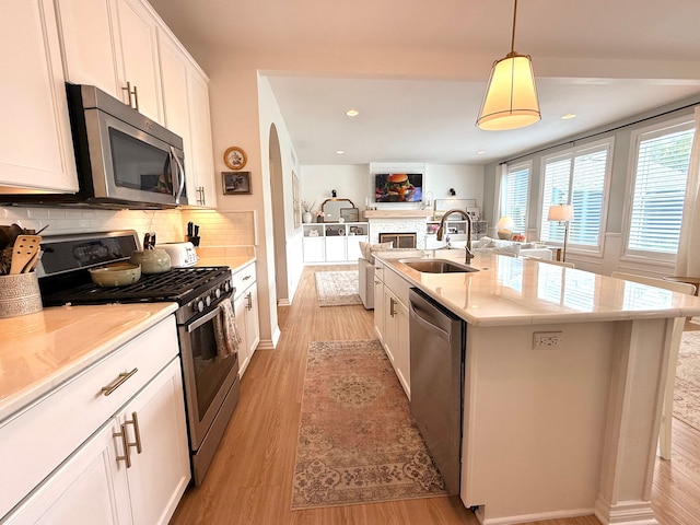 kitchen featuring appliances with stainless steel finishes, a sink, light wood-style floors, open floor plan, and backsplash