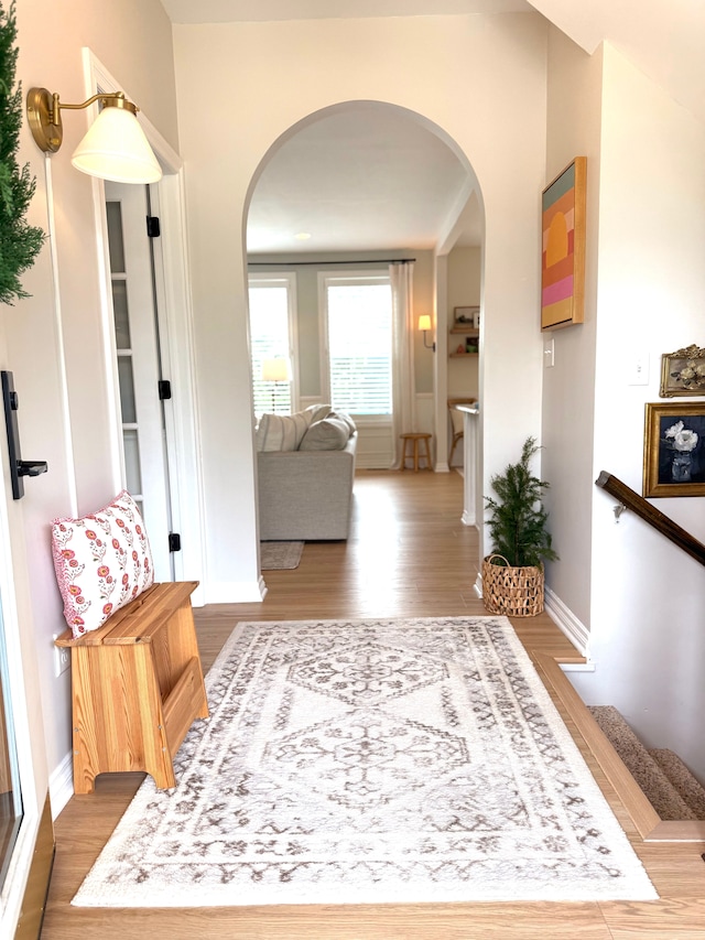 hall with arched walkways, baseboards, and wood finished floors