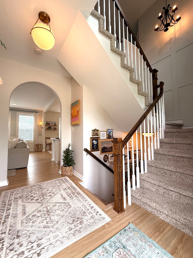 stairway with lofted ceiling, wood finished floors, baseboards, arched walkways, and a notable chandelier