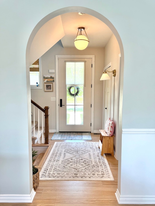 interior space featuring arched walkways, baseboards, wood finished floors, and stairway