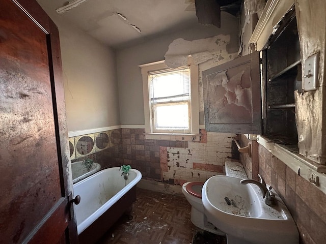 bathroom with wainscoting, a freestanding tub, toilet, tile walls, and a sink
