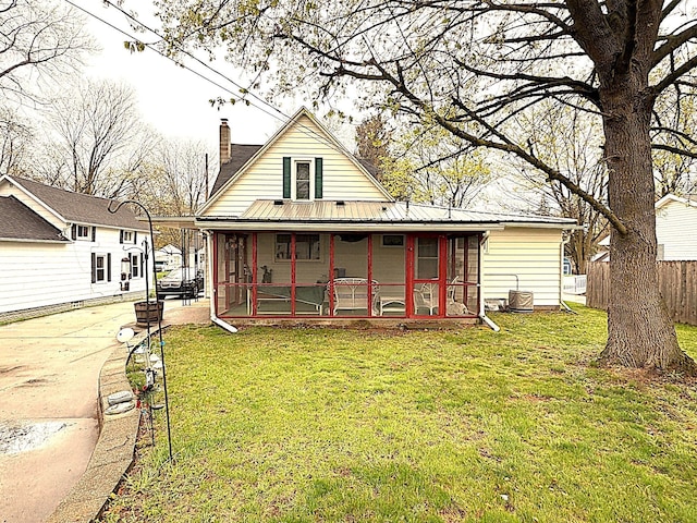 back of house with fence, a chimney, a lawn, covered porch, and metal roof