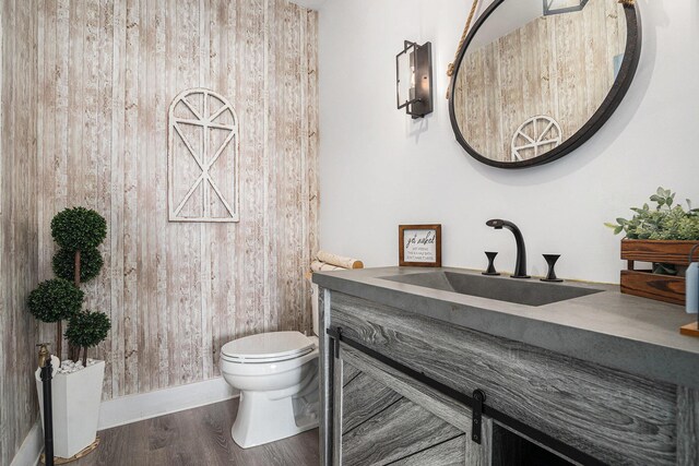 half bathroom featuring vanity, baseboards, wood finished floors, and toilet