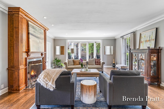 living area with baseboards, a high end fireplace, wood finished floors, and ornamental molding