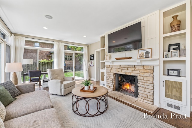 living room featuring visible vents, wood finished floors, a stone fireplace, baseboards, and built in shelves