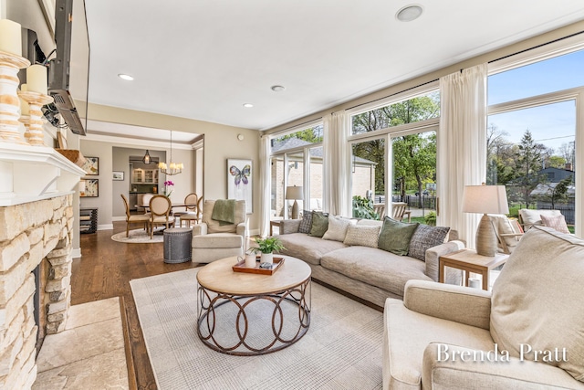 living room featuring a chandelier, dark wood-style floors, a stone fireplace, and a wealth of natural light