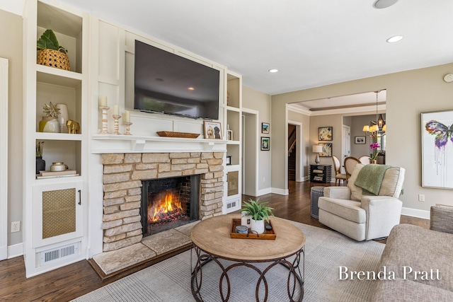 living room featuring a fireplace, built in shelves, wood finished floors, baseboards, and a notable chandelier