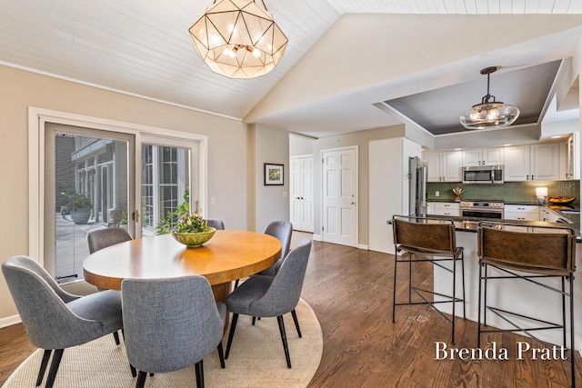dining area with dark wood-style flooring, a notable chandelier, and vaulted ceiling