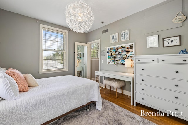 bedroom with an inviting chandelier, baseboards, wood finished floors, and visible vents