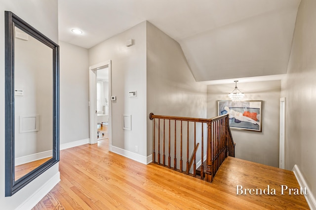 hallway featuring vaulted ceiling, an upstairs landing, wood finished floors, baseboards, and a chandelier