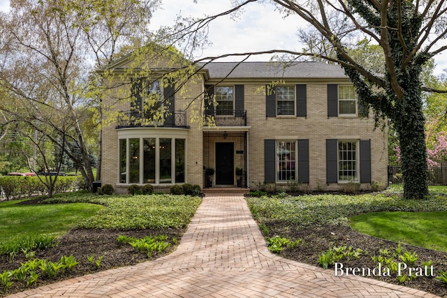 colonial house with a balcony, fence, and brick siding