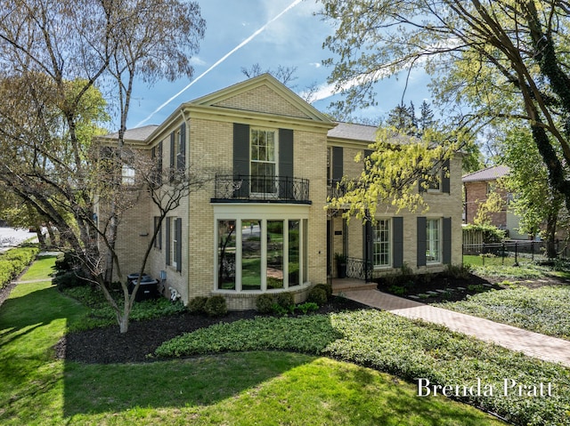 traditional-style home with brick siding, fence, a balcony, and a front lawn