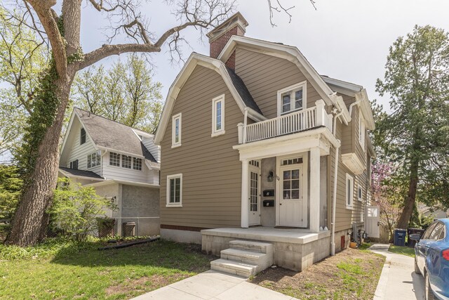 view of front of house with a gambrel roof, a front yard, a balcony, and a chimney