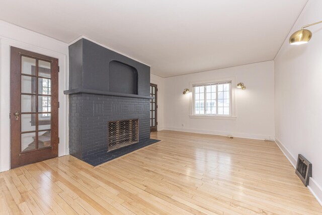 unfurnished living room featuring baseboards, a brick fireplace, wood finished floors, and visible vents