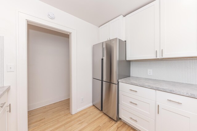 kitchen featuring light countertops, freestanding refrigerator, white cabinetry, light wood-type flooring, and tasteful backsplash