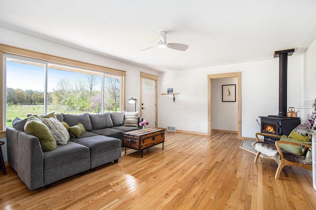 living area featuring ceiling fan, visible vents, a wood stove, baseboards, and light wood-style floors