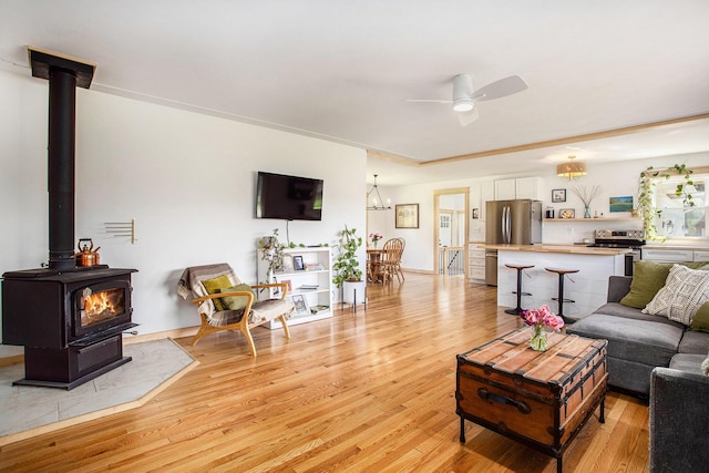 living area featuring ceiling fan, a wood stove, and light wood-style flooring