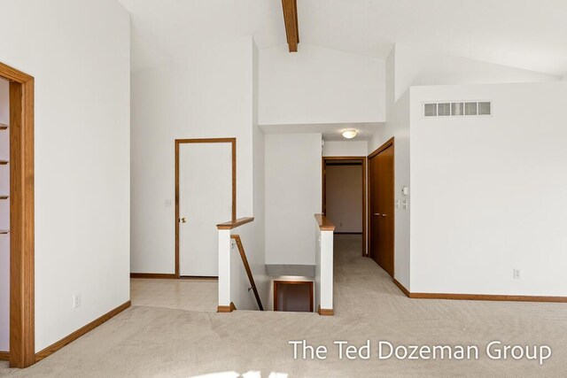 hallway featuring visible vents, carpet, baseboards, and beam ceiling