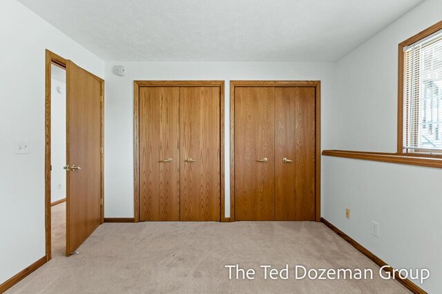 unfurnished bedroom with baseboards, carpet, and two closets
