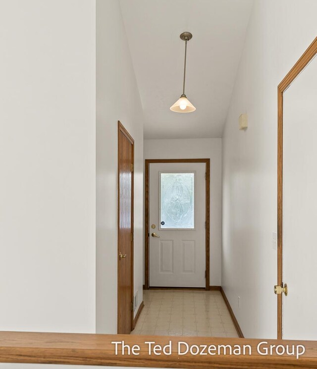 doorway featuring baseboards, vaulted ceiling, and light floors