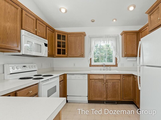 kitchen featuring visible vents, vaulted ceiling, brown cabinets, a sink, and white appliances
