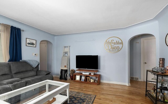 living area with arched walkways, baseboards, wood finished floors, and visible vents