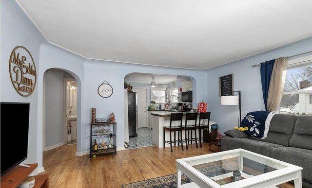 living room featuring arched walkways, ceiling fan, baseboards, and light wood-style floors