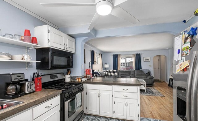 kitchen featuring arched walkways, a peninsula, dark countertops, and stainless steel appliances